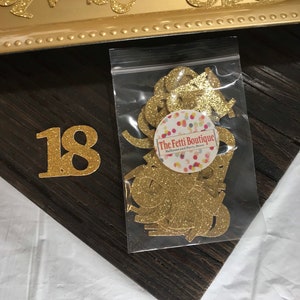 Puede incluir: Recortes de n&uacute;meros 18 de purpurina dorada en una bolsa de pl&aacute;stico transparente con una etiqueta blanca que dice "The Fetti Boutique - Decoraci&oacute;n de globos y fiestas".