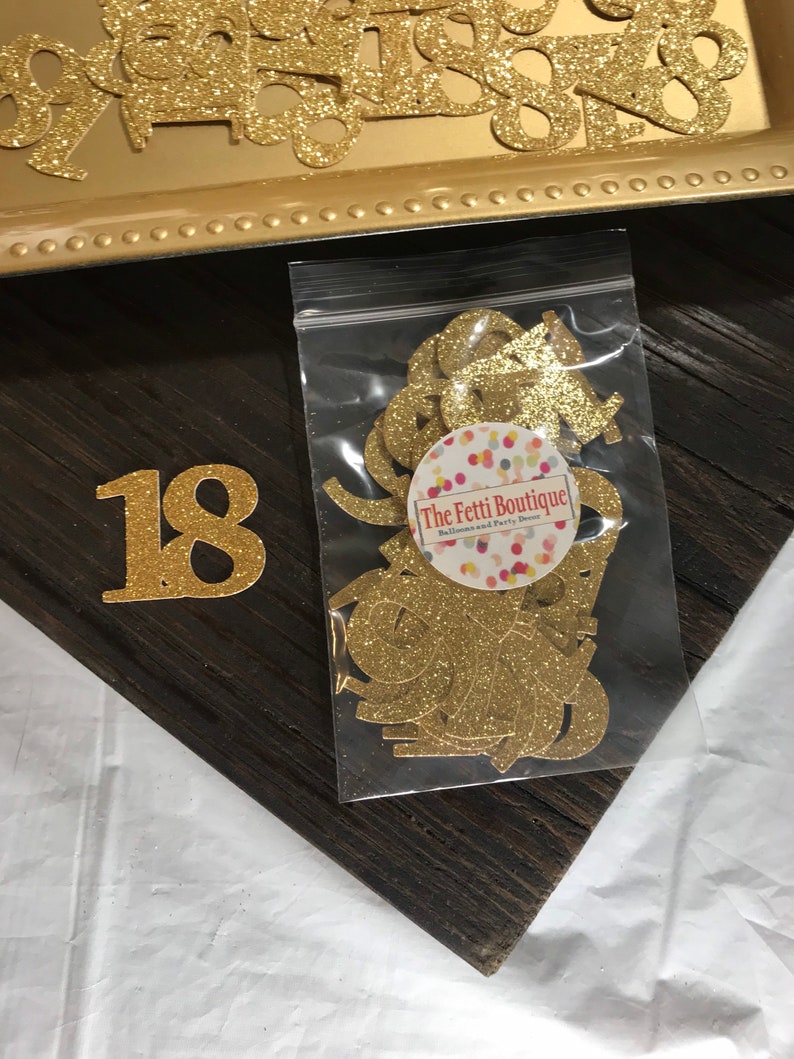 Puede incluir: Recortes de n&uacute;meros 18 de purpurina dorada en una bolsa de pl&aacute;stico transparente con una etiqueta blanca que dice "The Fetti Boutique - Decoraci&oacute;n de globos y fiestas".