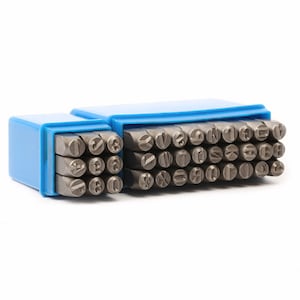 May include: A set of metal letter and number stamps in a blue plastic storage case. The stamps are arranged in rows and columns, with each stamp having a different letter or number. The case is open, revealing the stamps.