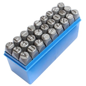 May include: A set of metal letter stamps arranged in a blue plastic storage container. The stamps are gray and have various capital letters engraved on their flat surfaces. The container is rectangular and has a slightly angled design.