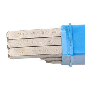 May include: A set of metal stamps with the text "MADE IN CHINA" and the number "6 mm" printed on each. The stamps are in a blue plastic case. The stamps are silver in color.