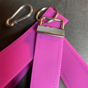 May include: A pink silicone keychain with a silver metal clasp and a silver ring. The keychain has a stitched edge.