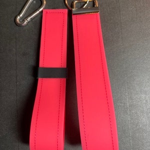 May include: Two pink keychains with black stitching and silver key rings. The keychains are made of a soft, flexible material.