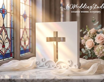 May include: A white square plaque featuring a central cutout cross and decorative scrollwork at the base. The plaque is positioned on a marble surface with draped fabric. The text "leWeddingStudio EXCLUSIVE WEDDING ACCESSORIES" is visible.