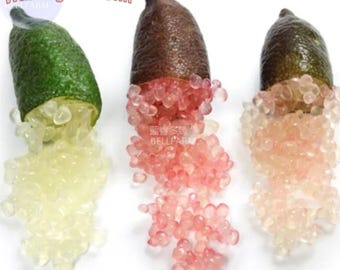 Puede incluir: Tres limas de dedo, una verde, una marrón y una morada, se cortan por la mitad para revelar sus semillas rosadas y blancas como caviar.