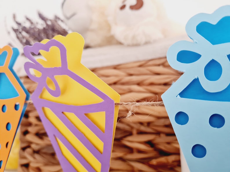 May include: A string of paper party decorations with a blue, yellow, and purple color scheme. The decorations are shaped like party hats and are connected by a twine string.