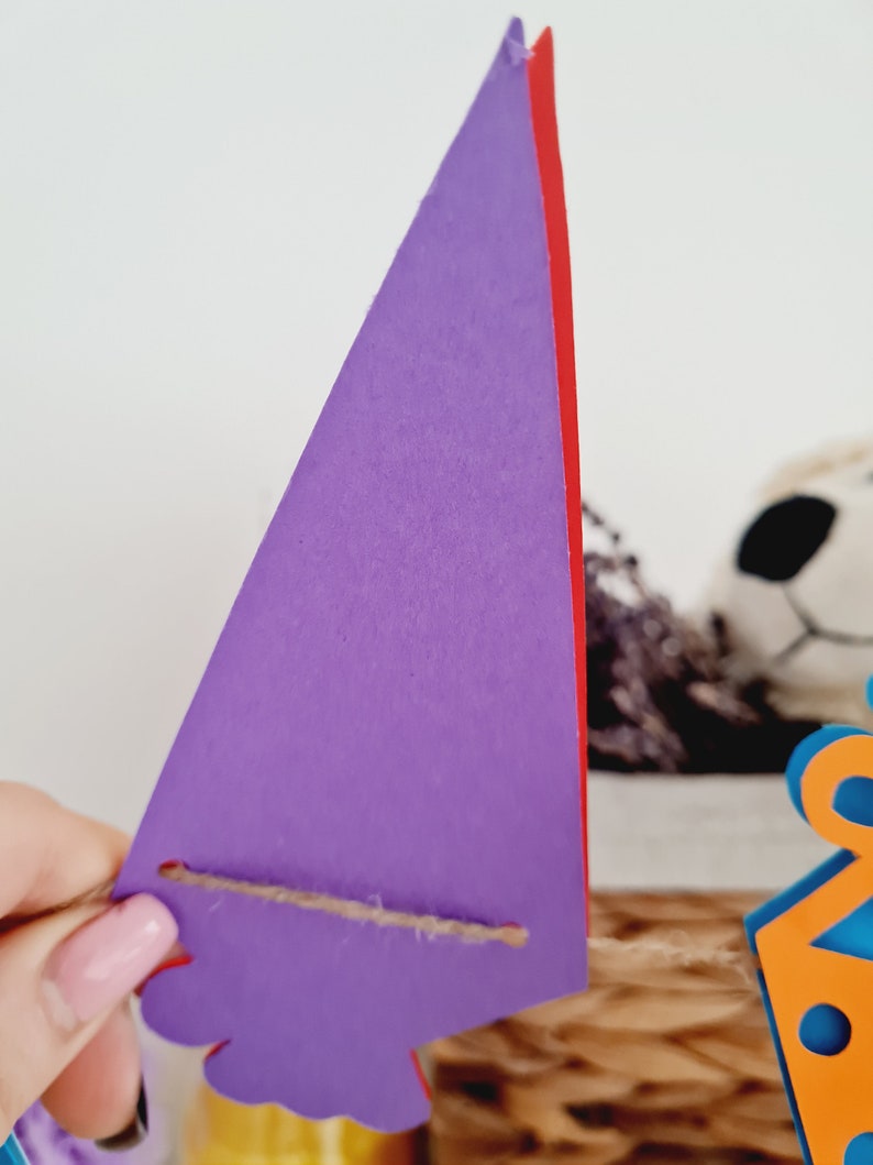 May include: Purple triangle banner with a red edge and a brown string attached. The banner is hanging from a string.