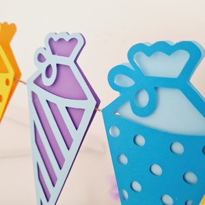 May include: A colorful paper garland with three pennants shaped like cones. The pennants are decorated with polka dots, stripes, and a bow. The garland is perfect for a birthday party or other celebration.