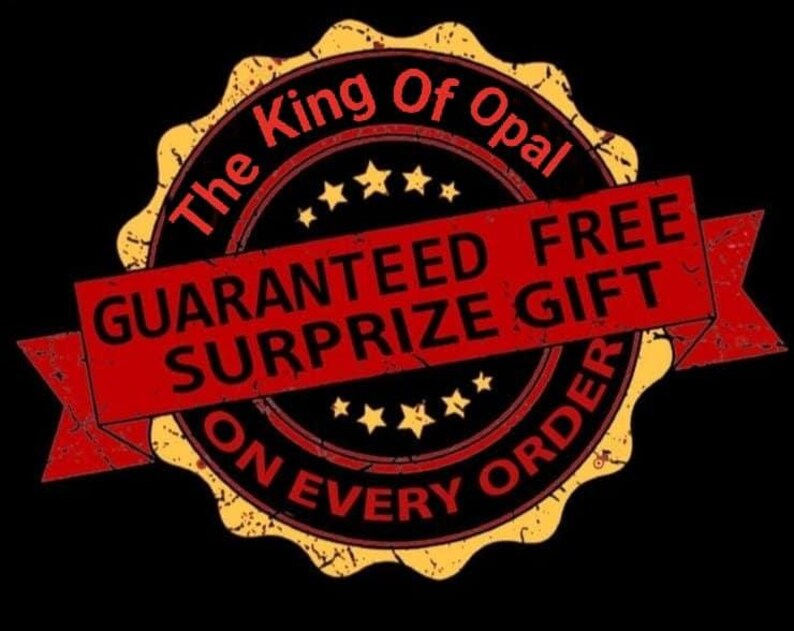 May include: A distressed, circular emblem with the text "The King Of Opal" in a black and red design. A red banner across the center reads "GUARANTEED FREE SURPRIZE GIFT ON EVERY ORDER". The emblem has a gold border and star accents.