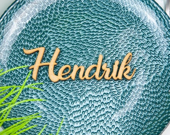 May include: A teal blue plate with a textured surface and the name "Hendrik" written in cursive on it with wooden letters.
