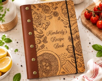 May include: A wooden recipe book with a brown leather spine secured by six brass-colored rivets. The cover features laser-engraved illustrations of food and kitchen tools, with the text "Kimberly's Recipe Book" centered and a black elastic band.