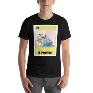 May include: A black t-shirt featuring a cartoon illustration of a man fixing a toilet. The image is within a yellow frame with the text "59" and "EL PLOMERO" in black.