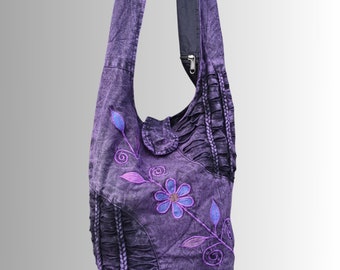 May include: Purple cotton shoulder bag with a floral design embroidered in pink and blue. The bag has a zipper closure and a ruffled trim.
