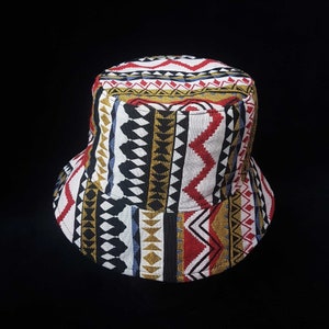 Op de afbeelding: Een bucket hat met een geometrisch patroon in zwart, wit, rood, goud en blauw.