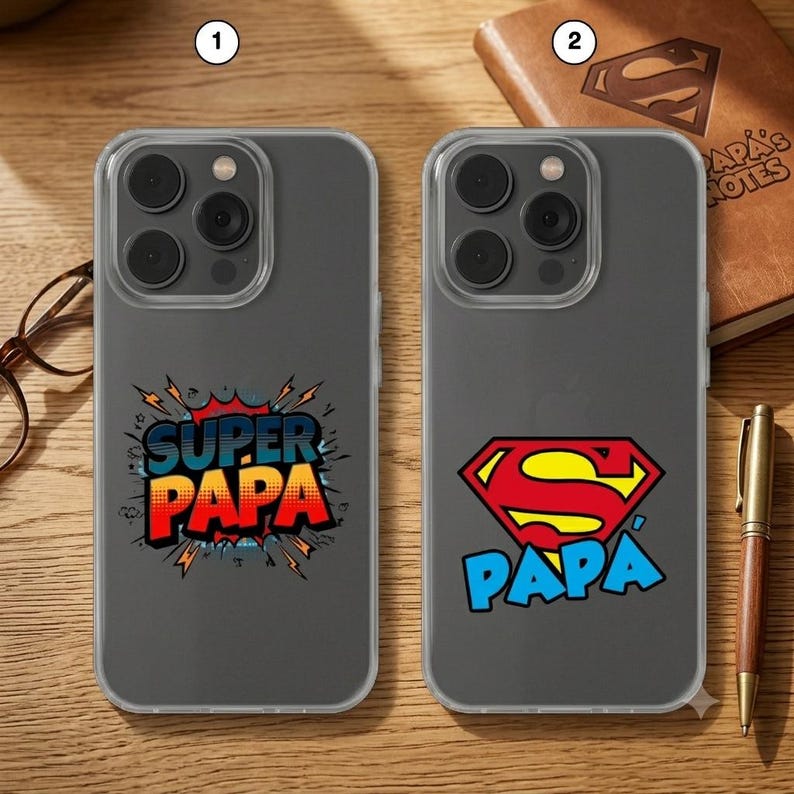 May include: Two clear smartphone cases featuring graphic designs. The first case displays the text SUPER PAPA in a comic-book style burst. The second case features a red and yellow Superman-style shield logo above the blue text PAPA.