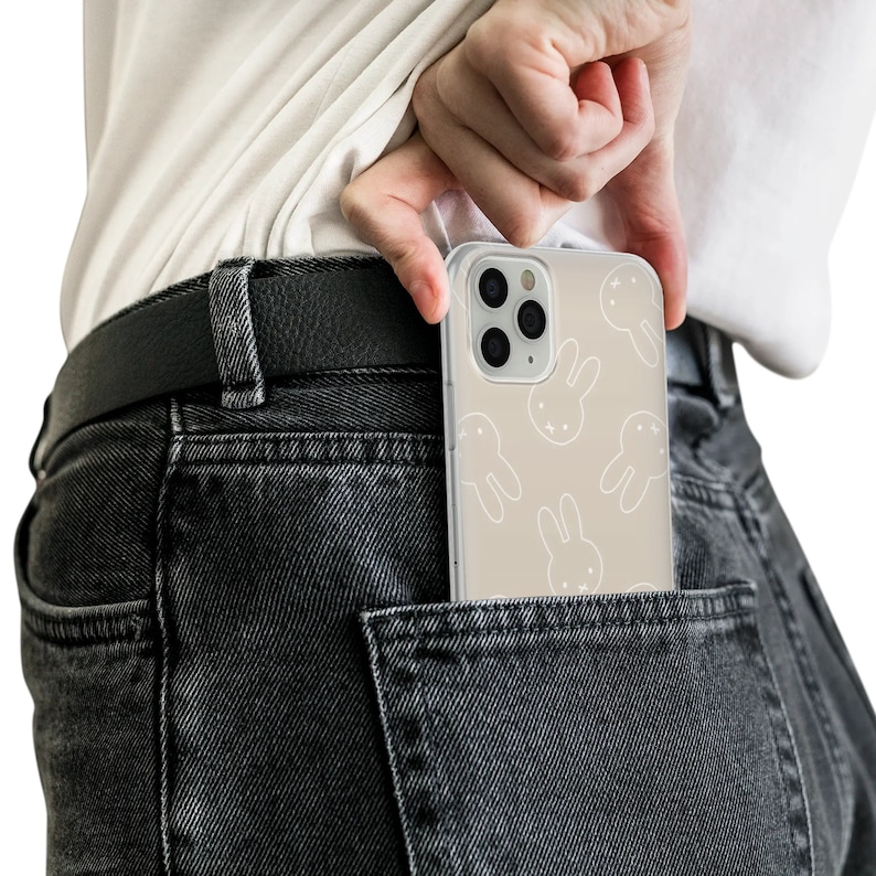 May include: A clear phone case with a light brown background and white bunny rabbit silhouettes. The case is in the back pocket of a pair of dark gray jeans.