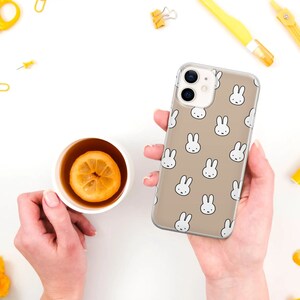May include: A clear phone case with a beige background and a repeating pattern of white bunny faces.
