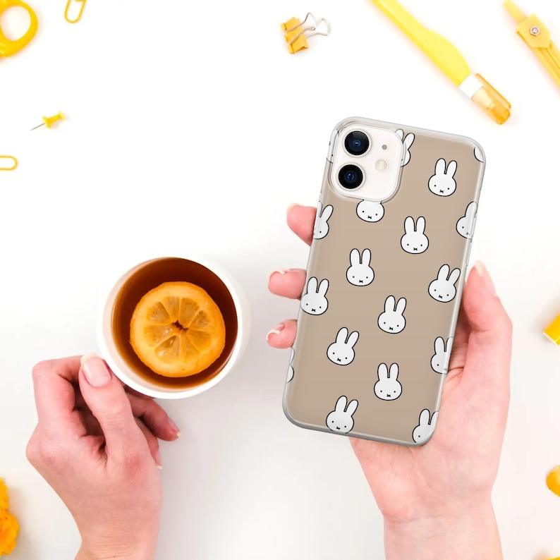 May include: A clear phone case with a beige background and a repeating pattern of white bunny faces.
