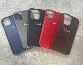 May include: Five rectangular smartphone cases in navy blue, grey, black, red, and dark brown, each featuring a textured surface and a square camera cutout. Each case is personalised with gold-coloured embossed initials: M.A, L.O, D.M, S.W, and CBM.