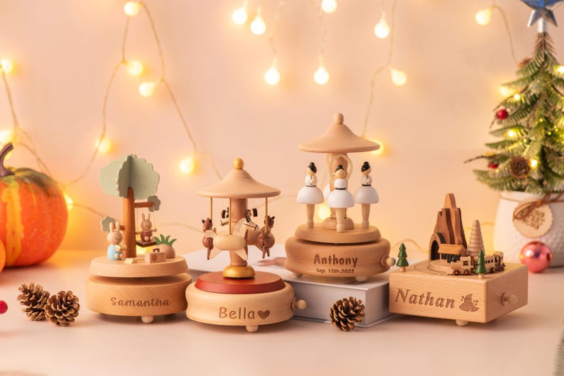 May include: Wooden music boxes with personalized names, including a carousel, a tree with rabbits, and a ballerina design. The boxes are light brown with decorative elements and are set against a warm, festive background.