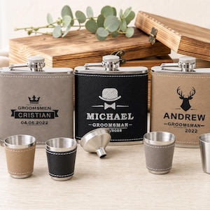 May include: Three rectangular metal flasks wrapped in grey, black, and tan leather-like material, each engraved with names, dates, and icons. Four small metal shot cups, some with matching leather sleeves, and a small metal funnel are arranged in front.