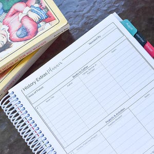 Puede incluir: Un planificador encuadernado en espiral con el t&iacute;tulo "History Extras Planner" y una pila de libros antiguos. El planificador tiene separadores con pesta&ntilde;as y p&aacute;ginas rayadas para notas. Los libros se titulan "Little House in the Big Woods" y "Farmer Boy".