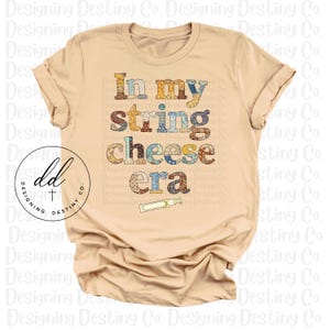 May include: A beige t-shirt featuring the phrase "In my string cheese era" in a variety of patterned fonts. A small string cheese illustration is below the text. The shirt has short sleeves and a round neck.
