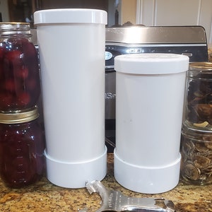 May include: Two white plastic jars with lids, one taller than the other, and two glass jars with gold lids, one stacked on top of the other, filled with preserved fruit and mushrooms.