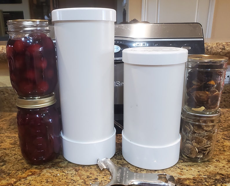 May include: Two white plastic jars with lids, one taller than the other, and two glass jars with gold lids, one stacked on top of the other, filled with preserved fruit and mushrooms.