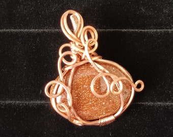 May include: A handcrafted pendant featuring a sparkling, golden-brown stone encased in intricate copper wire. The wire is artfully shaped into decorative swirls and loops, creating a unique and eye-catching jewelry piece.