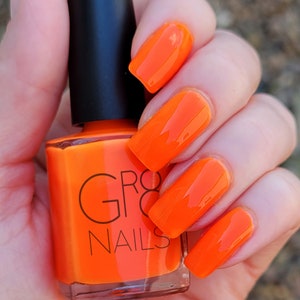 May include: A bottle of bright orange nail polish with a black cap is held in a hand with matching orange polished nails. The nail polish bottle has the brand name "GRO8 NAILS" printed on it.