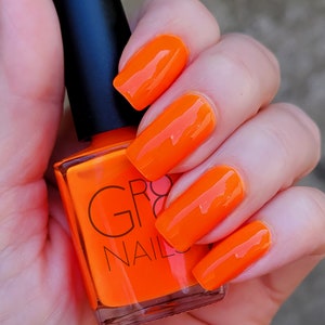May include: Bright orange nail polish and matching nail color. The nail polish bottle has a black cap and the brand name "GR8 NAILS" printed on the front. The nails are long and rectangular, with a glossy finish.