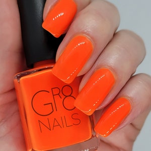 May include: Bright orange nail polish and painted nails. The square bottle of nail polish has a black cap and the words "GR8 NAILS" printed on the front. The nails are a vibrant, glossy orange.