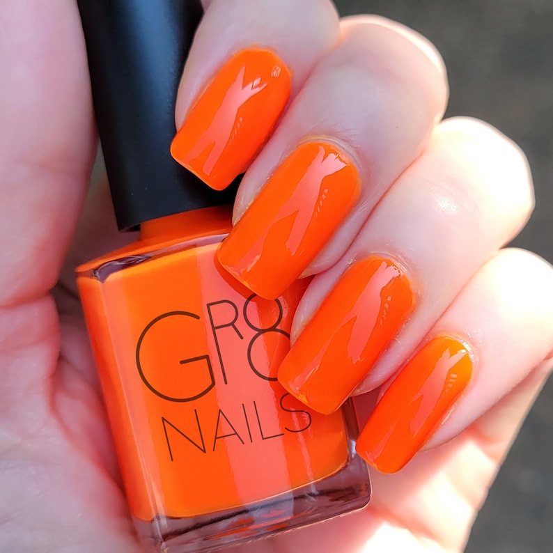 May include: Bright orange nail polish and matching manicure. The bottle of polish has a black cap and the brand name "GR8 NAILS" printed on the front. The nails are a glossy, solid orange color.