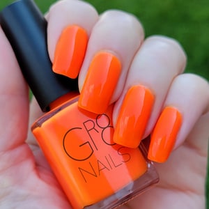 May include: Bright orange nail polish and matching nail color. The bottle of nail polish is held in a hand with painted nails. The brand name "GR8 NAILS" is printed on the bottle.