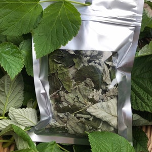 May include: A silver resealable pouch filled with dried green leaves. The pouch has a clear window to view the contents. The pouch is sitting on a bed of green leaves.