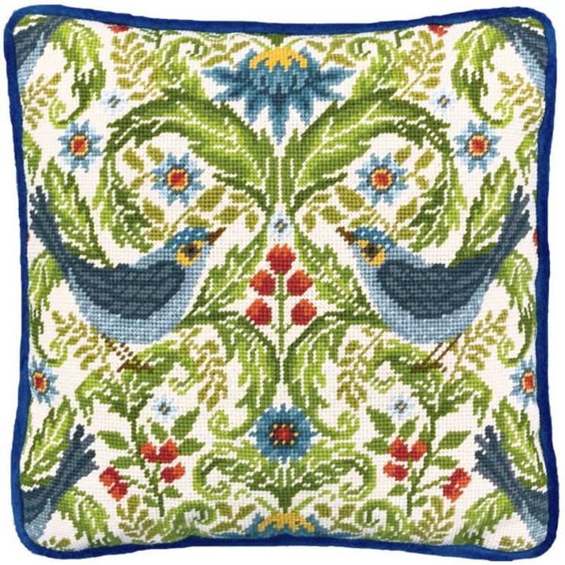 May include: A white pillow with a blue border features a repeating pattern of blue birds, green leaves, and red and blue flowers. The design is reminiscent of a traditional tapestry.