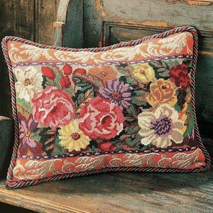 Puede incluir: Una almohada rectangular con un diseño floral. La almohada presenta una variedad de flores en tonos de rojo, rosa, amarillo, blanco y morado. La almohada está rodeada por un borde decorativo.