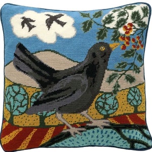 May include: A blackbird with a yellow beak sits on a branch with red berries. The bird is looking up at two black birds flying in the sky. The background is a blue sky with white clouds and a green field.