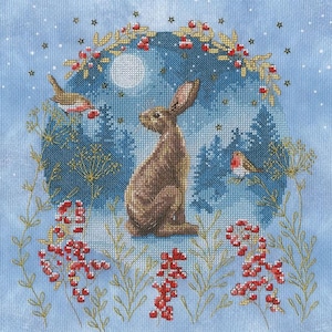 May include: A cross-stitch design featuring a brown hare seated in a winter scene. A full moon and evergreen trees are visible in the background. Red berries and birds are also featured in this nature-themed artwork.