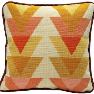 May include: A square throw pillow with a geometric pattern of orange, pink, and white triangles. The pillow has a brown border.