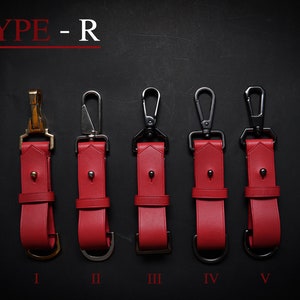 May include: Five red leather keychains with different metal clasps. The keychains are labeled I through V.