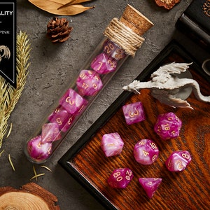 May include: A set of pink and white dice with gold numbers in a glass test tube with a cork stopper. The dice are on a wooden tray with a small grey dragon figurine. The text "IMMORTALITY SOUL WHITE + PINK" is on a black label.