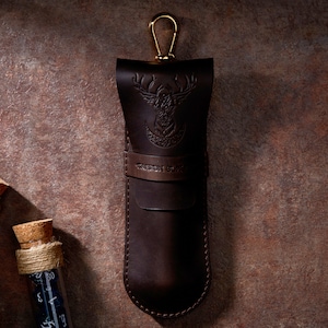 May include: A brown leather case with a gold metal clasp and a deer head design. The case has the text "GRIFFIN GUILD" embossed on the front.