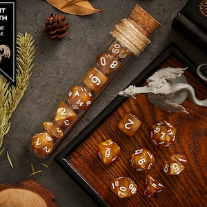 May include: A set of orange marble dice with white numbers in a glass test tube. The dice are in a wooden box with a miniature dragon figurine. The box has a dark brown wood grain finish.