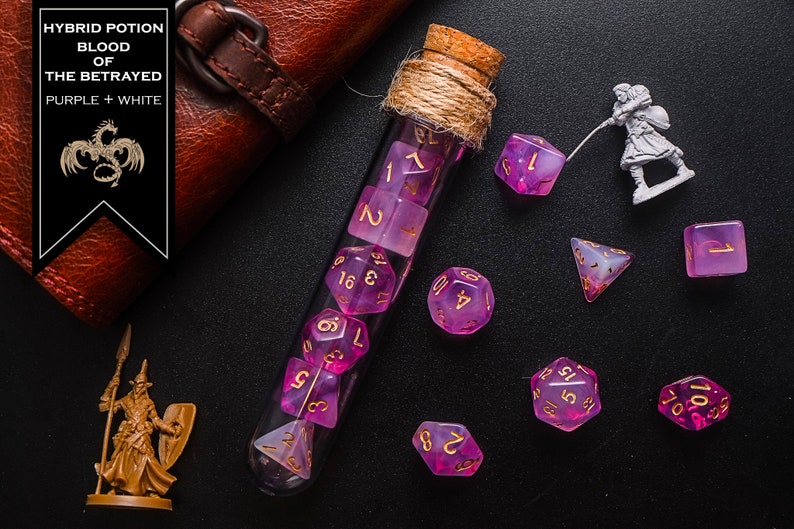 May include: A glass test tube filled with purple and white dice with gold numbers. The test tube is corked and tied with twine. The dice are scattered around the test tube on a black surface. The text "HYBRID POTION BLOOD OF THE BETRAYED PURPLE + WHITE" is on a black label.
