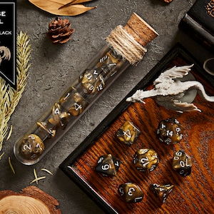 May include: A set of gold and black dice in a glass tube with a cork stopper. The dice are in a wooden tray with a small dragon figurine. The dice are labelled with numbers 1 through 20.
