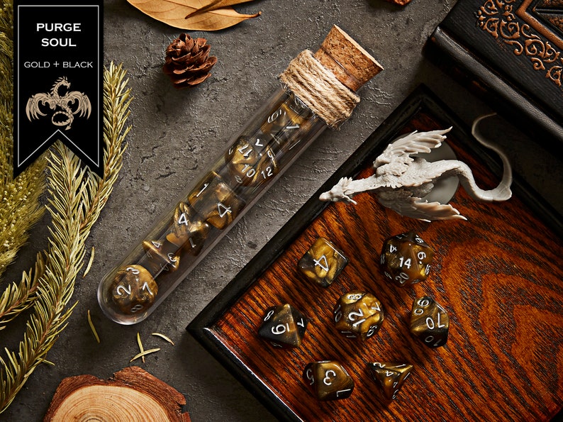 May include: A set of gold and black dice in a glass tube with a cork stopper. The dice are in a wooden tray with a small dragon figurine. The dice are labelled with numbers 1 through 20.