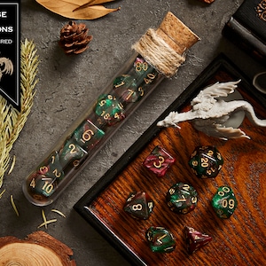 May include: A set of green and red dice with gold numbers in a glass test tube with a cork stopper. The dice are on a wooden tray with a small dragon figurine.