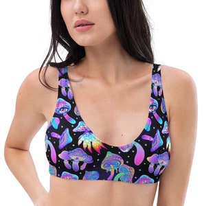 May include: A black bikini top with a vibrant, psychedelic mushroom pattern. The design features colorful mushrooms, stars, and an eye motif in shades of blue, purple, and green. The top has a scoop neckline and wide straps.